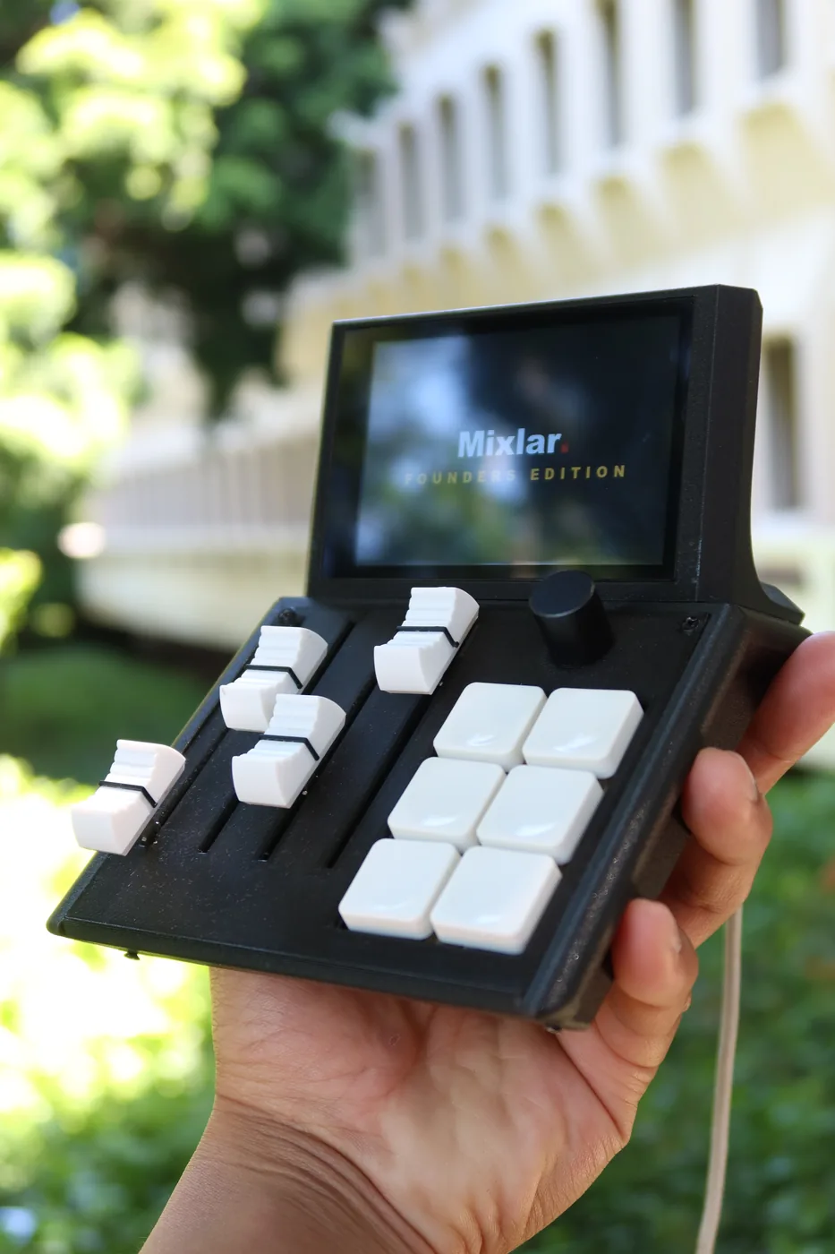 Mixlar M1X held in hand outdoors, screen showing the Founders Edition splash
