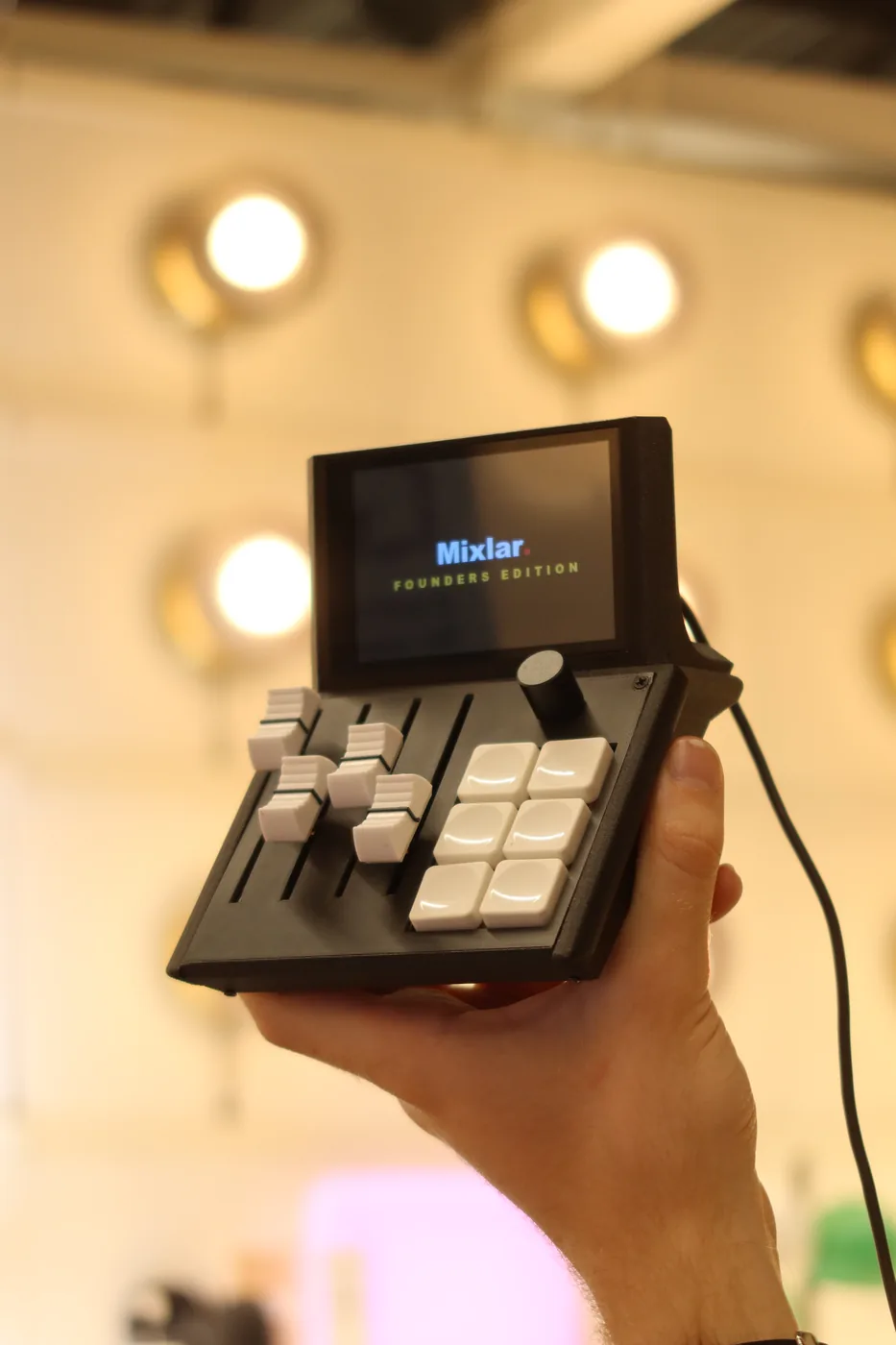 Mixlar M1X held in hand, screen lit, warm gallery lighting behind
