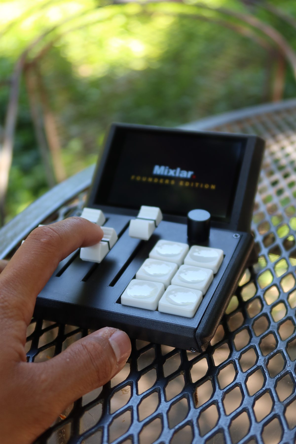 A hand resting on a Mixlar M1X outdoors, its screen showing the Mixlar Founders Edition splash.
